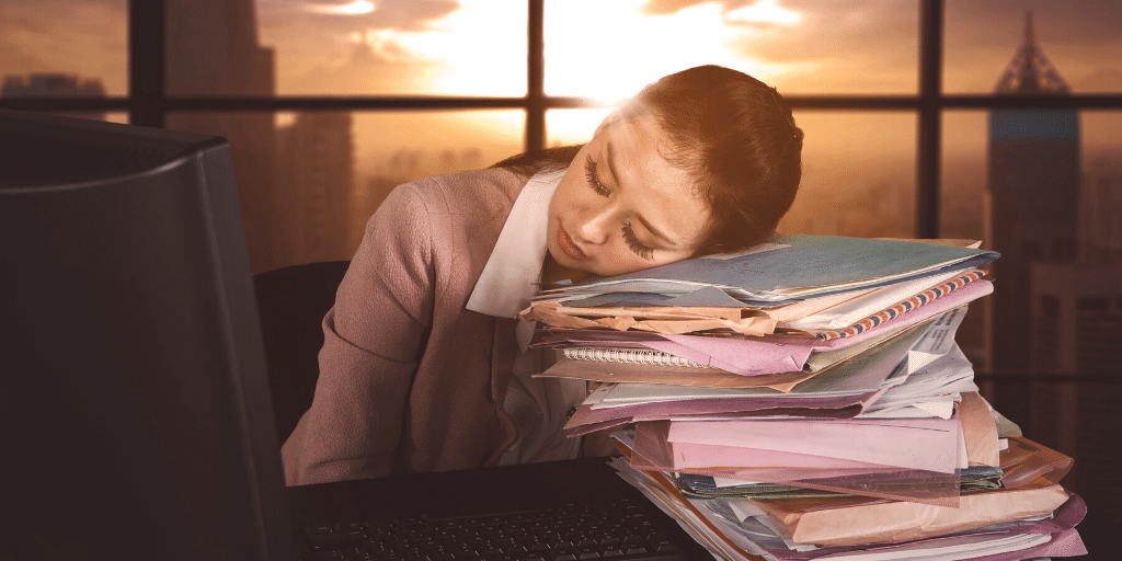 Overworked woman asleep at desk as sun comes up